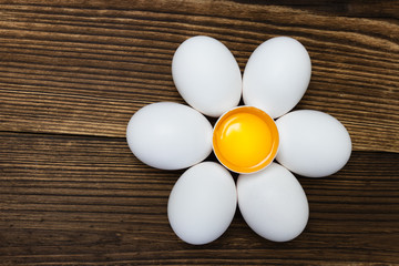 Chicken white eggs laid out around a broken egg in the form of a chamomile on a wooden background. Easter