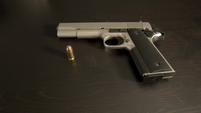 Cocked pistol with .45 ACP bullet standing on table, wide center shot