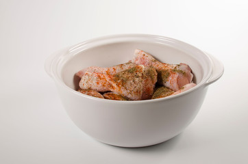 Raw chicken drumsticks marinated in spices in a large white ceramic saucepan with a lid