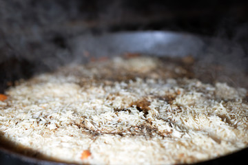 cooking Rice for pilaw or paella in iron cauldron over open fire. Smoke and steam. Tasty food preparing outdoor process background