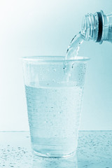 Pouting of pure mineral water from plastic bottle into transparent glass or cup