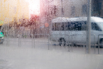 Drops of water flow down the windowpane. Waking the weather outside the window. Cars drive on a wet road. Abstract background