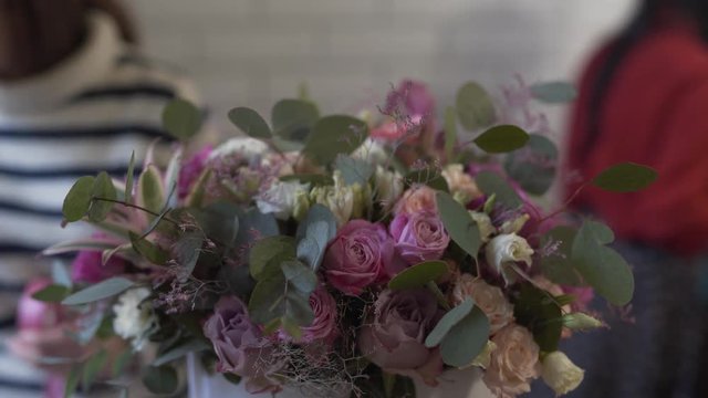 Close-up picture of a bunch of violet and white roses with green euqalyptus in round box. A bouquet is being made by florist in flower shop.