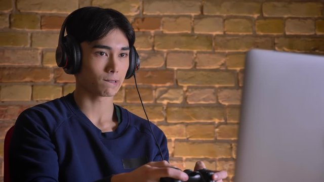 Closeup portrait of young attractive korean man in headphones playing video games indoors