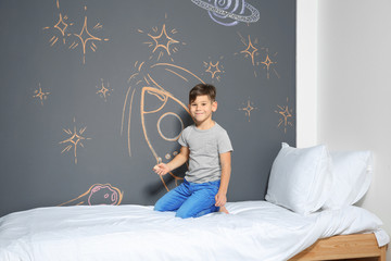 Little child drawing rocket with chalk on wall in bedroom
