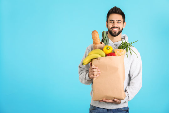 Man holding paper bag with fresh products on color background, space for text. Food delivery service