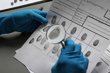 Criminalist exploring fingerprints with magnifying glass at table, closeup
