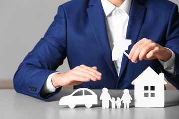 Male insurance agent covering paper family, car and home with umbrella cutout at table, closeup