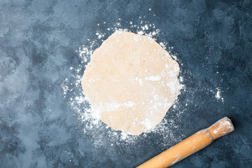 Female hands rolling dough on a table with a wooden rolling pin. Top view. Flat lay.