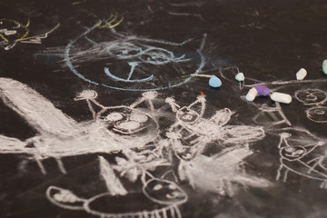 Many small and large cats are drawn with chalk on a black chalk surface by the hand of a child. Children's sketch flock of lynx on the  blackboard.