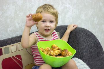A little boy in a striped t-shirt appropriated a bowl of cupcakes and eats out one by one.