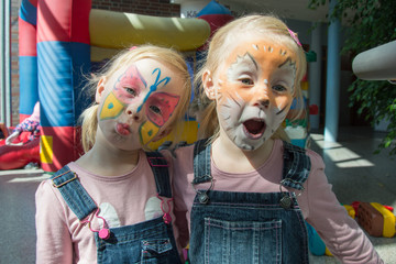 two little girls with brightly decorated faces of a butterfly and a lion cub, having fun at a...