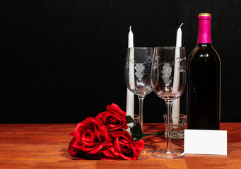 Beautiful etched wine glasses and bottle of red wine, white candles and red roses on wooden table...