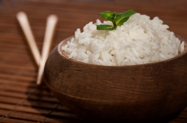 Cooked white rice in wooden bowl with chopsticks on the wood brown bamboo background.