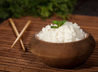 Cooked white rice in wooden bowl with chopsticks on the wood brown bamboo background.