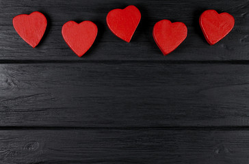 Fototapeta na wymiar The romantic background with red wooden hearts on a black wooden background.