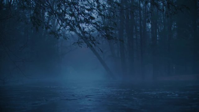 Moody blue mist and fog shroud a flooding river overflowing its banks at dusk