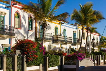 Fototapeta na wymiar Colorful buildings with palm trees and flowers on sunny day in Puerto de Mogan, Gran Canaria. Summer vacation, travel destination in Canary Islands, Spain