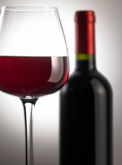 Close-up of a glass filled with red wine, with a red wine bottle in the background