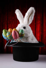 White rabbit coming out of magician's hat with a bunch of decorated easter eggs