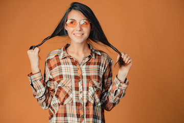 Cute young brunette girl in check shirt playing with hair on orange background
