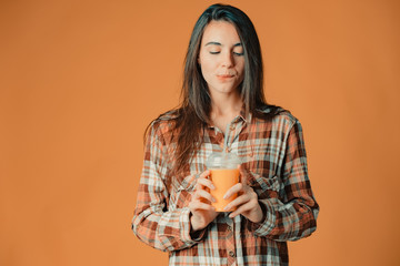 Cute caucasian young brunette girl holding orange juice on orange background