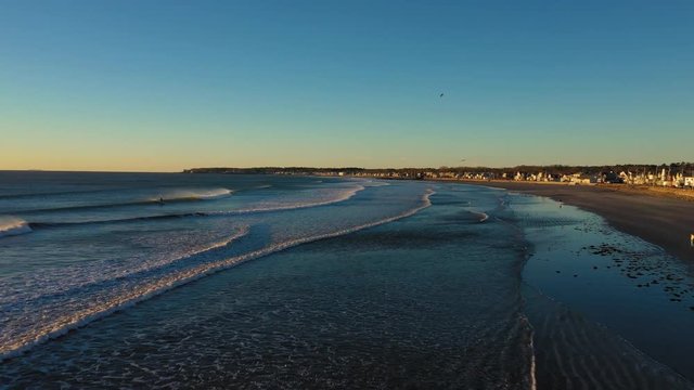 Aerial footage of a cold December morning in York Beach Maine flying out over the ocean with surfers and seagulls enjoying the water