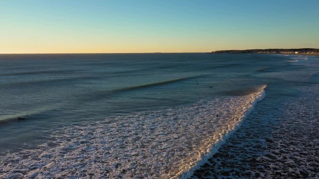 Stationary aerial footage of a waves heading to shore while 4 surfers wait and a seagull flies towards shore on a cold December morning in York Beach Maine