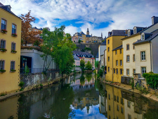 Fototapeta na wymiar Colorful houses in the Alzette river in old town (Grund district) of Luxembourg, with beautiful reflections in the water and Saint Michael's Church (Eglise Saint-Michel) at the top
