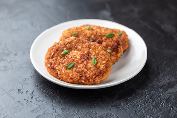 Cutlets lie on a white plate. Chicken cutlets lie among the vegetables on a black stone table.