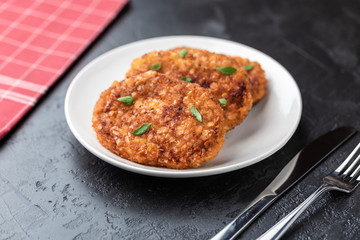 Cutlets lie on a white plate. Chicken cutlets lie among the vegetables on a black stone table.