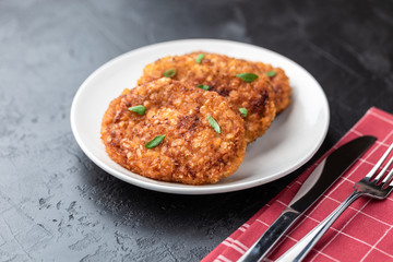 Cutlets lie on a white plate. Chicken cutlets lie among the vegetables on a black stone table.