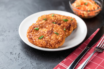 Cutlets lie on a white plate. Chicken cutlets lie among the vegetables on a black stone table.