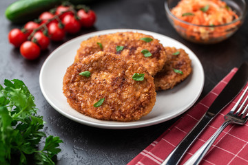 Cutlets lie on a white plate. Chicken cutlets lie among the vegetables on a black stone table.