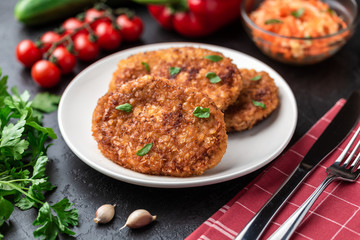 Cutlets lie on a white plate. Chicken cutlets lie among the vegetables on a black stone table.