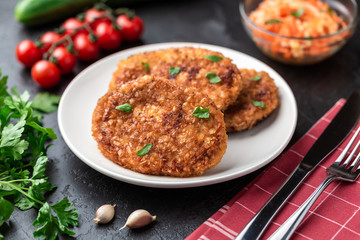 Cutlets lie on a white plate. Chicken cutlets lie among the vegetables on a black stone table.