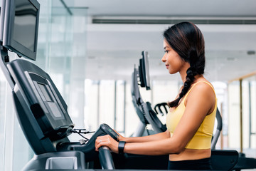 Fototapeta na wymiar Attractive Asian woman smiling and running on a running treadmill at gym. Fitness model giving thumbs up