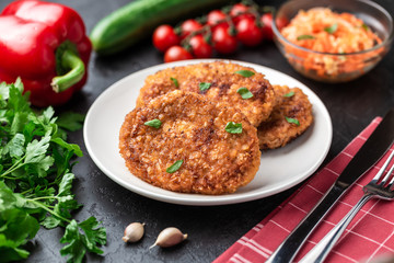 Cutlets lie on a white plate. Chicken cutlets lie among the vegetables on a black stone table.