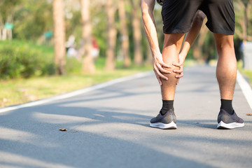 Young fitness man holding his sports leg injury. muscle painful during training. Asian runner...