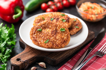 Cutlets lie on a white plate. Chicken cutlets lie among the vegetables on a black stone table.