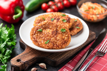 Cutlets lie on a white plate. Chicken cutlets lie among the vegetables on a black stone table.