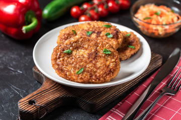 Cutlets lie on a white plate. Chicken cutlets lie among the vegetables on a black stone table.