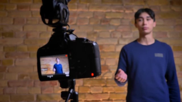 Closeup shoot of camera recording korean male videoblogger talking and then refocusing on the speaker