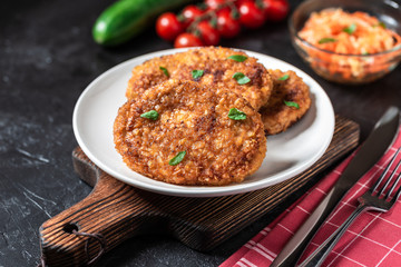 Cutlets lie on a white plate. Chicken cutlets lie among the vegetables on a black stone table.