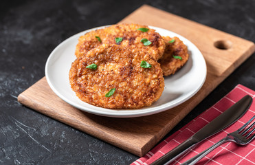 Cutlets lie on a white plate. Chicken cutlets lie among the vegetables on a black stone table.