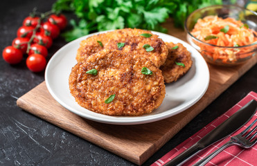 Cutlets lie on a white plate. Chicken cutlets lie among the vegetables on a black stone table.