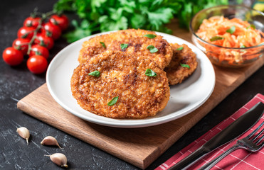 Cutlets lie on a white plate. Chicken cutlets lie among the vegetables on a black stone table.