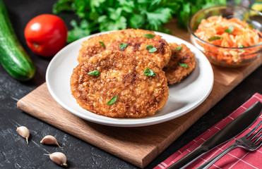 Cutlets lie on a white plate. Chicken cutlets lie among the vegetables on a black stone table.