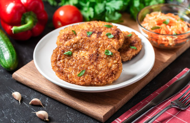 Cutlets lie on a white plate. Chicken cutlets lie among the vegetables on a black stone table.