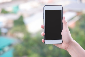 hand holding smartphone or mobile phone with city building background and copy space.
